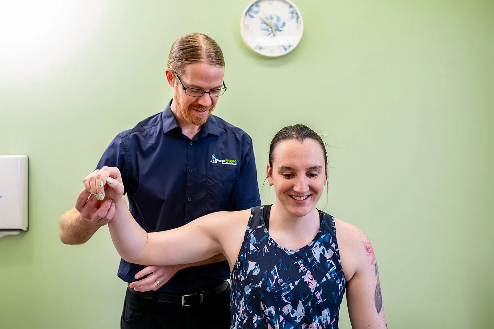 A physiotherapist guiding a smiling patient through a shoulder movement